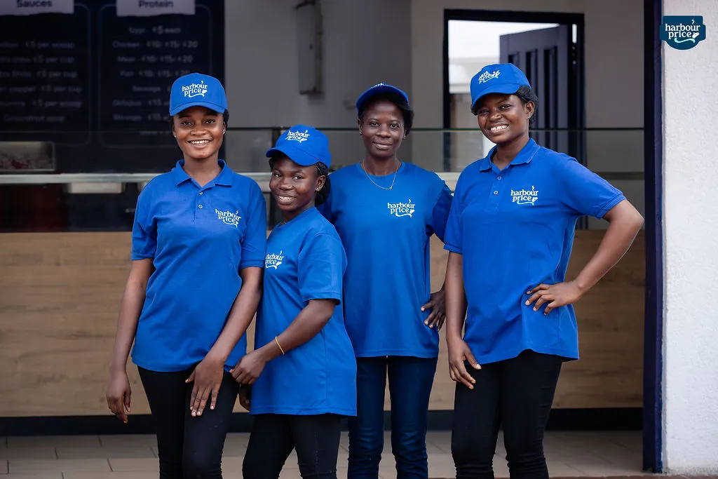 Four members of the Harbour Price team in royal-blue shirts and caps, smiling outside the Hot Meals counter