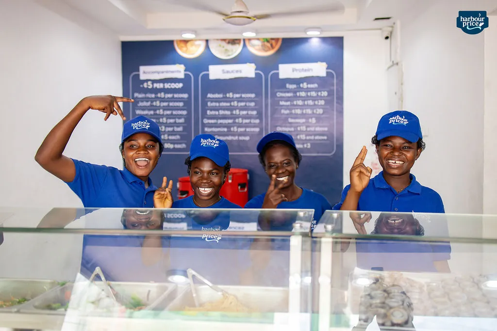 The Hot Meals crew in royal blue caps smiling behind the food counter