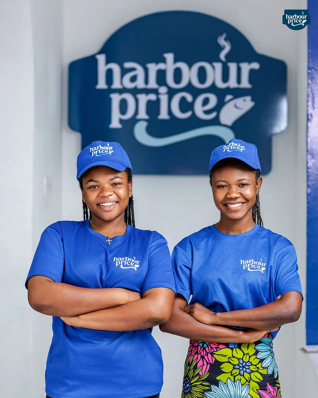Two smiling Harbour Price staff in royal blue caps and shirts under the store's logo sign