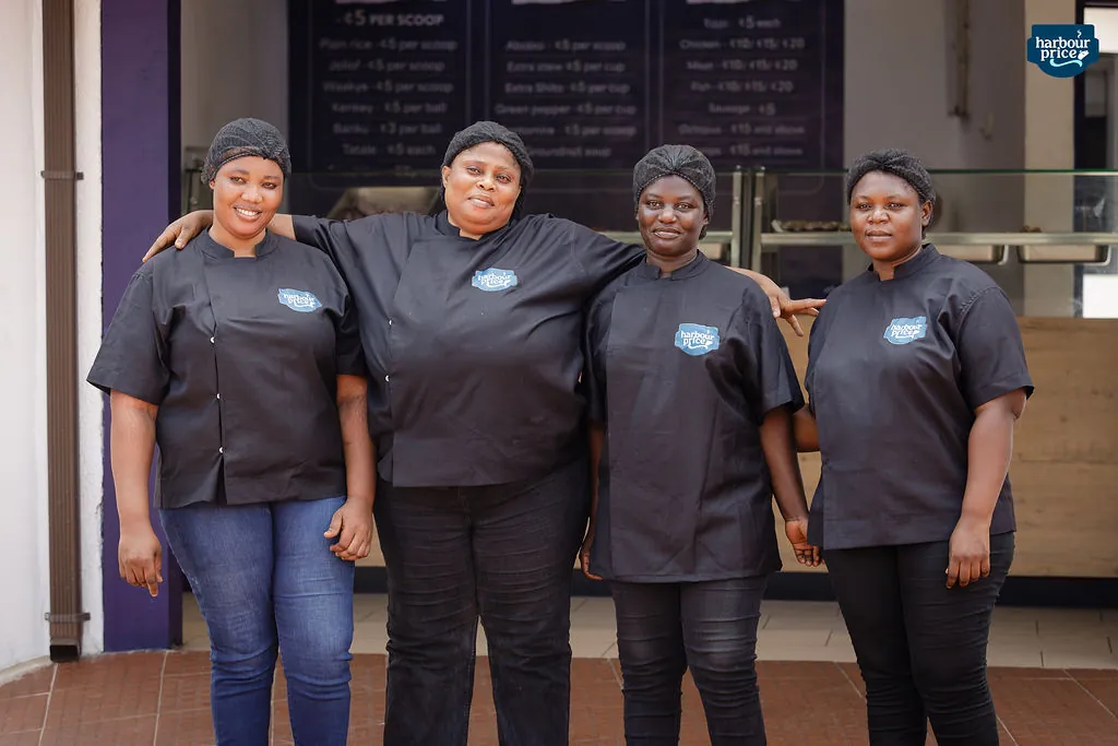 Harbour Price chefs in black uniforms and hairnets smiling outside the kitchen
