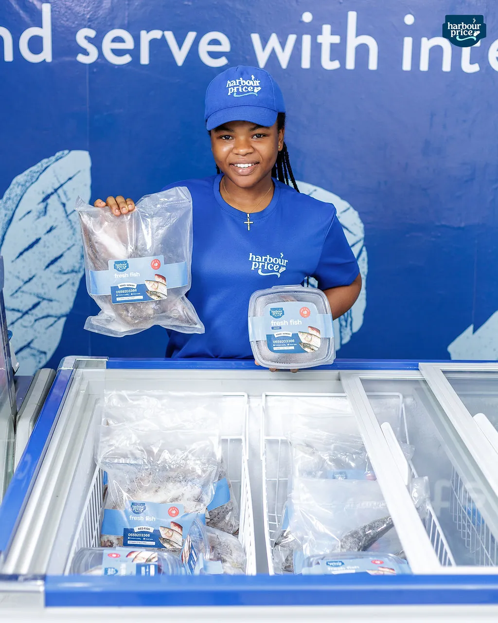 A smiling Harbour Price staffer holds up packs of frozen fish at the cold store freezer