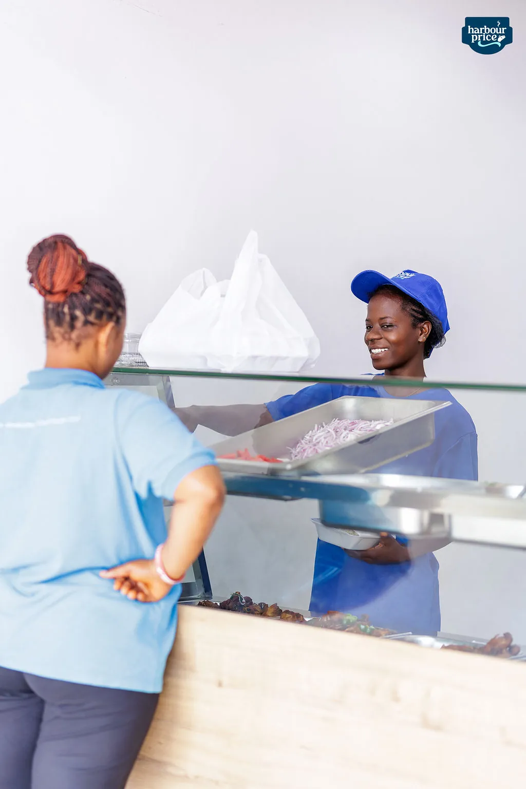 A Hot Meals server smiling as she hands a customer her order across the counter
